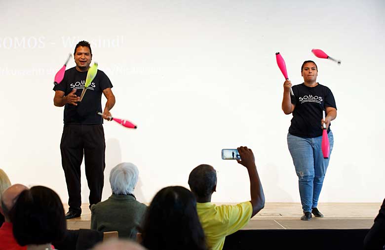 zwei Personen stehen auf einer Bühne und jonglieren.